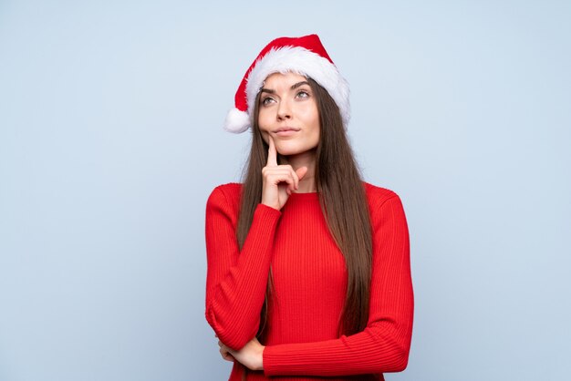 Girl with christmas hat over isolated blue thinking an idea