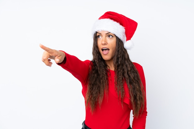 Girl with christmas hat over isolated white background pointing away