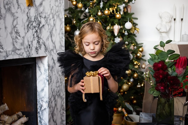 メリー クリスマスとハッピー ホリデー ライトとクリスマス ツリーの近くに彼女の手でクリスマス プレゼントを持つ少女