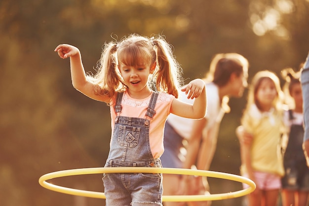 Girl with circle fitness tool. Group of kids have active weekend in the field. Illuminated by beautiful sunlight.