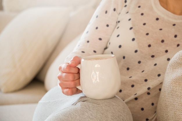 Girl with coffee mug sitting on the sofa indoors Woman drinking a cup of coffee or tea sitting cozy at home Relax and rest