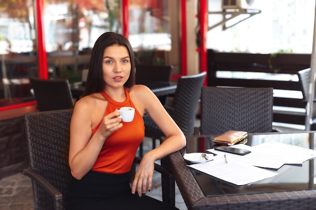 Girl With a cup of coffee sitting in a cafe. Wide smile. Beautiful clean skin. Business woman after signing documents. Business meeting.