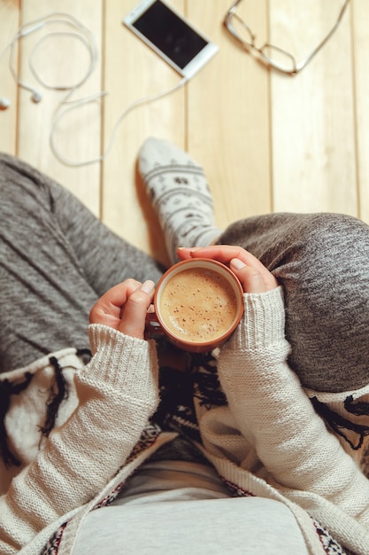 Foto ragazza con una tazza di caffè che si siede su una vista dall'alto del pavimento in legno