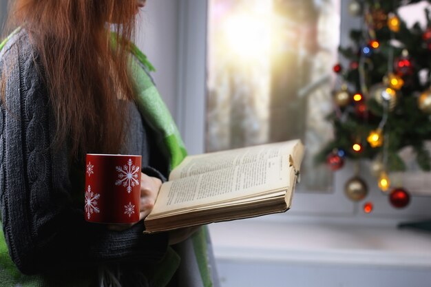 La ragazza con una tazza di bevanda calda sta davanti a una finestra a capodanno