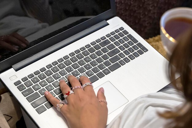 Girl with a cup of tea in her hand is typing on a laptop