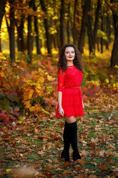 Girl with curls in a red dress in the autumn forest