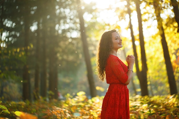 Girl with curls in a red dress in the autumn forest