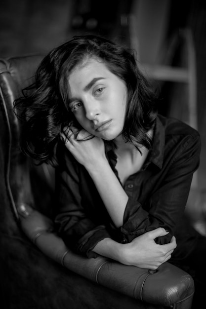 Girl with curly dark hair and natural makeup sitting on a dark leather chair black and white photo