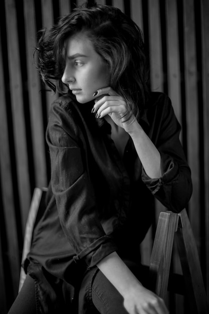 Girl with curly dark hair and natural makeup sitting on a dark leather chair black and white photo