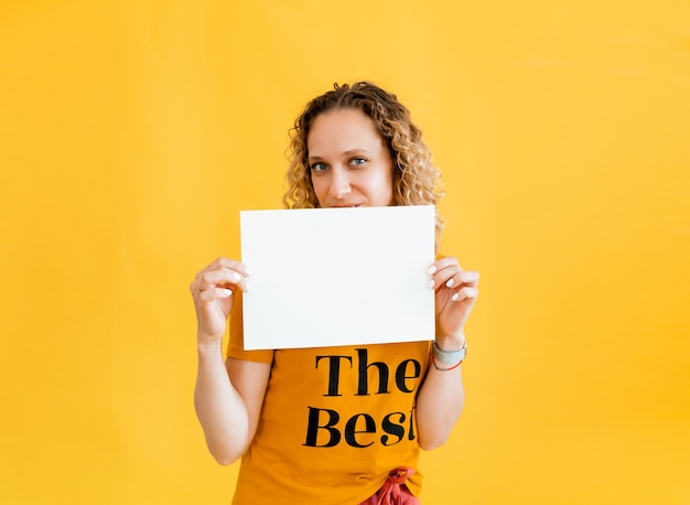 Girl with curly hair holding a blank card. Isolated on yellow background smiling woman portrait.