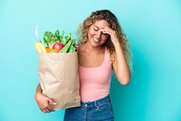 Girl with curly hair holding a grocery shopping bag isolated on green background laughing