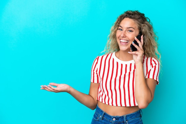 Girl with curly hair isolated on blue background keeping a conversation with the mobile phone with someone