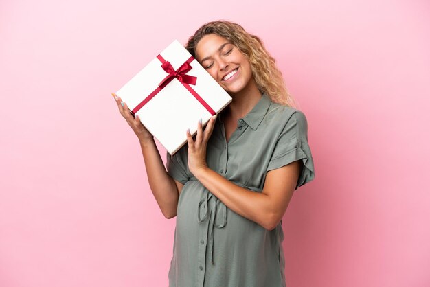 Girl with curly hair isolated on pink background pregnant and holding a gift