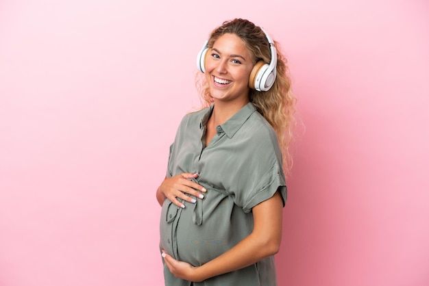 Girl with curly hair isolated on pink background pregnant and listening music