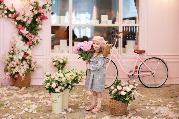 girl with curly hair sits at a table with a bouquet of pink peonies