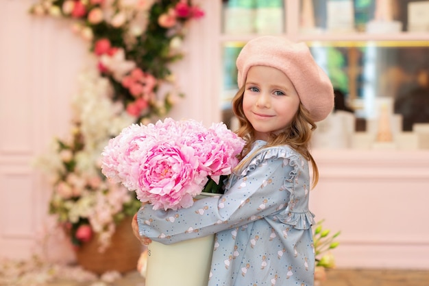 girl with curly hair sits at a table with a bouquet of pink peonies