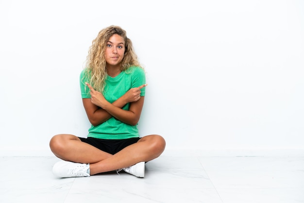 Girl with curly hair sitting on the floor pointing to the laterals having doubts