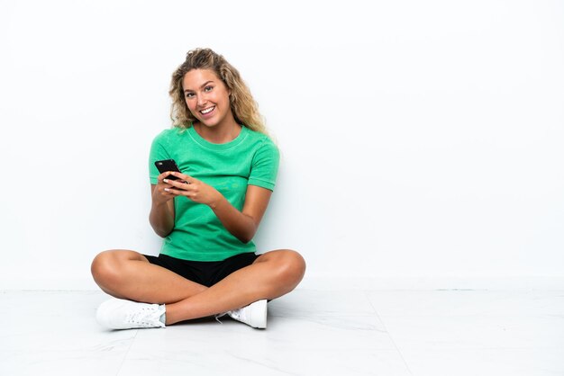 Girl with curly hair sitting on the floor sending a message with the mobile