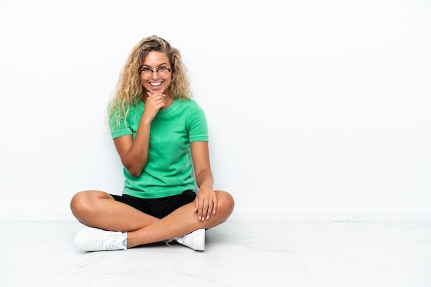 Girl with curly hair sitting on the floor with glasses and smiling