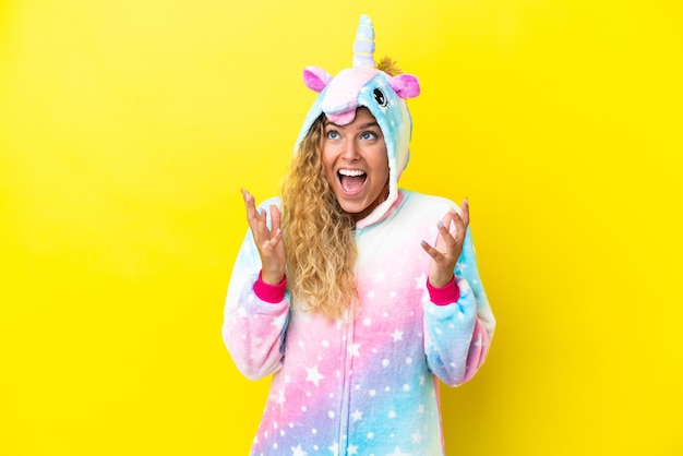 Girl with curly hair wearing a unicorn pajama isolated on yellow background with surprise facial expression