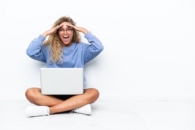 Foto ragazza con i capelli ricci con un computer portatile seduto sul pavimento con espressione sorpresa