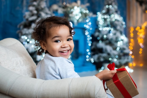 肌の色が濃い女の子がクリスマスツリーの下に横たわっています。かわいいムラートが新年を祝っています。アフリカの女の子、贈り物