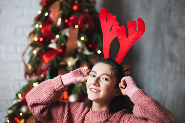 Girl with deer antlers on the background of the Christmas tree.