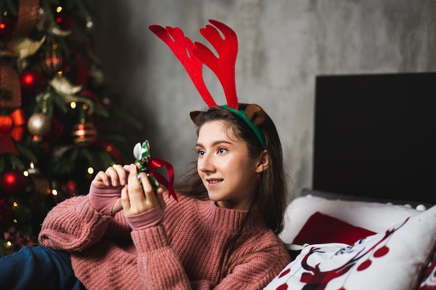 Girl with deer antlers on the background of the Christmas tree.