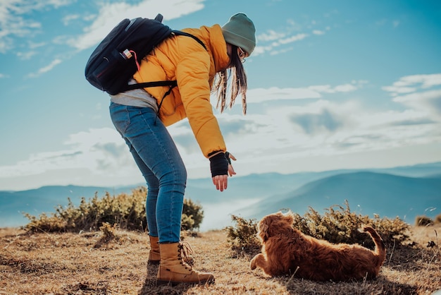 Девушка с собакой играет в горах. Осеннее настроение. Путешествие с домашним животным. Женщина и ее собака позируют на открытом воздухе.