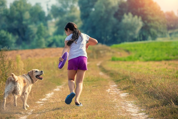 A girl with a dog runs along a dirt path in the field