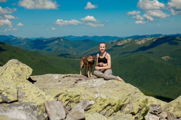 Девушка с собакой на вершине горы, наблюдая красивый пейзаж с широко открытыми руками