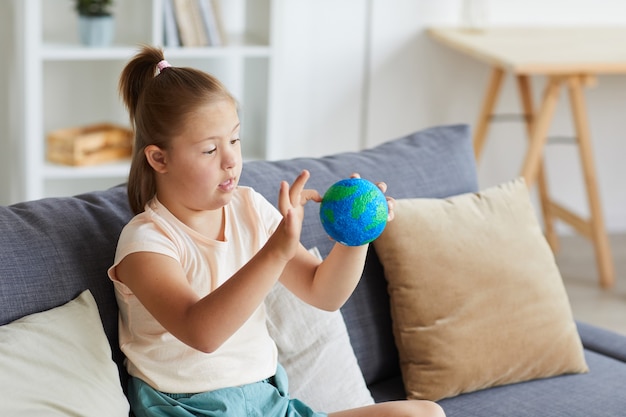 自宅のソファに座って地球惑星のモデルを調べるダウン症の少女