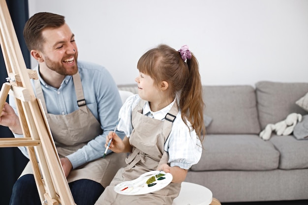 Girl with Down syndrome and her father painting on an easel with brushes