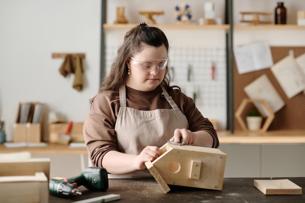 Girl with down syndrome making birdhouse from wood while working at table in workshop