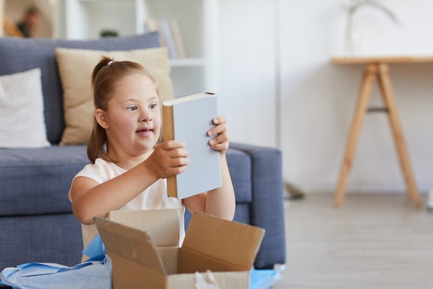 部屋に座っている間に箱から本を取り出すダウン症の少女