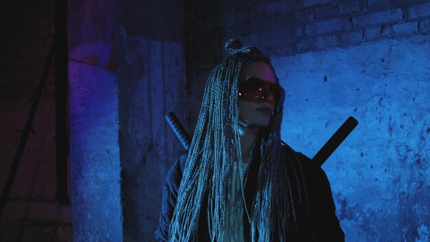 Girl with dreadlocks and katanas in red glasses posing against a neon brick wall