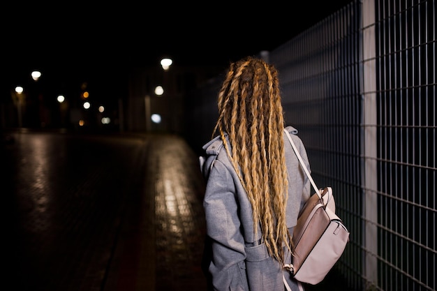 Girl with dreadlocks walking at night street of city