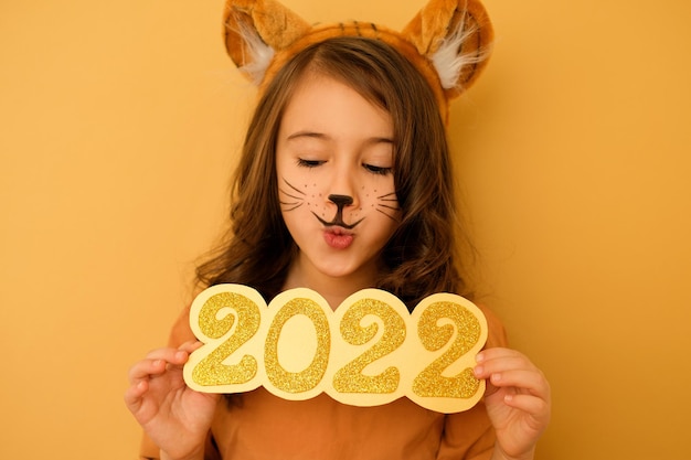 A girl with ears and tiger whiskers painted on face looks down in surprise at the numbers of 2022