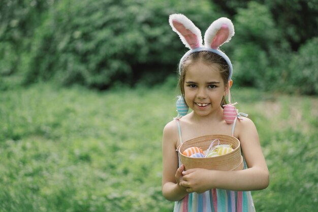 Girl with eggs basket and bunny ears on easter egg hunt in garden