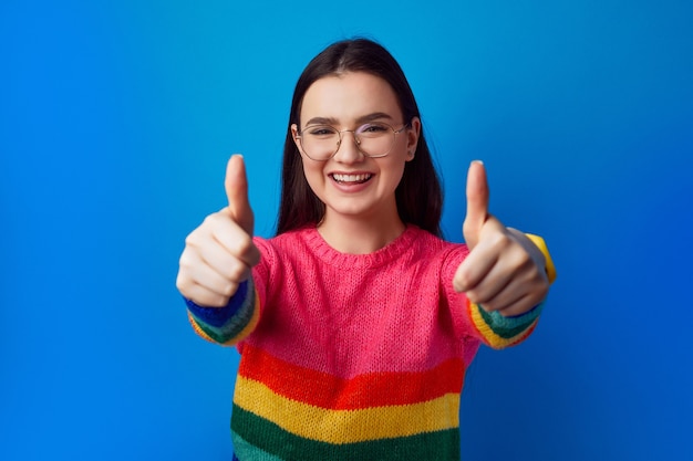 Girl with eyeglasses smiling and showing thumb up gesture with both hands