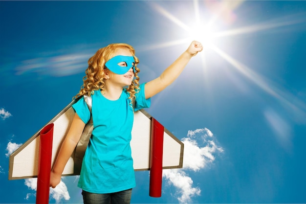 Girl with fake wings pretending to be pilot against sky