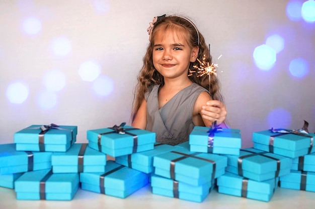 Girl with firework sparkler near a huge pile of blue gift boxes