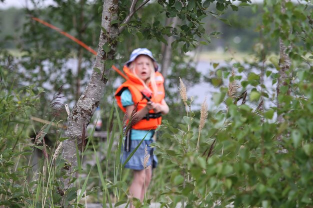 Photo girl with fishing rod standing by tree