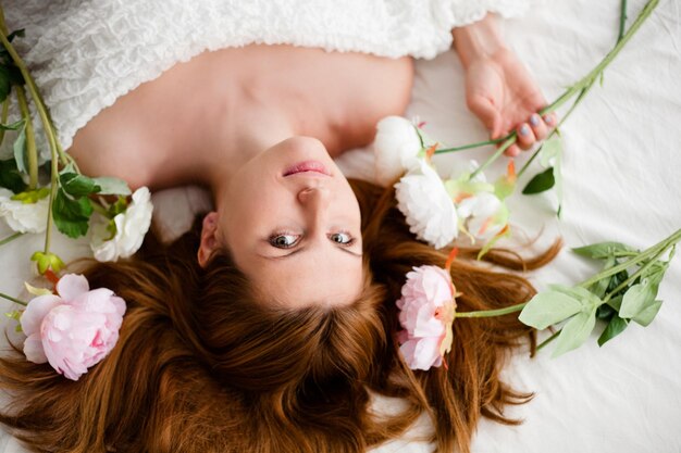 Girl with flowers on red hair lying in the bed