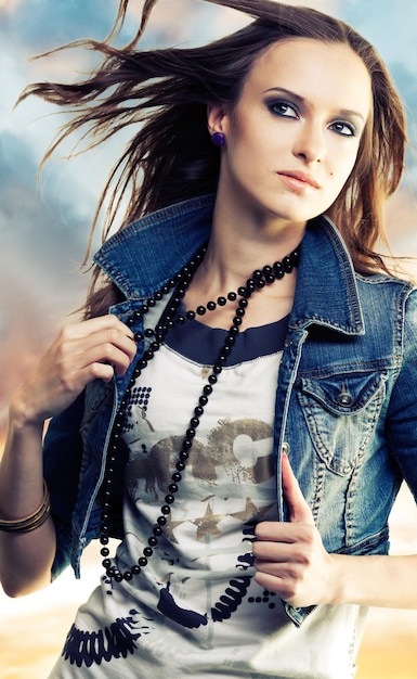 A girl with flying hair holding beads in jeans jacket on an abstract background