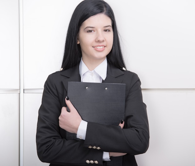 Girl with a folder stands near the white wall.