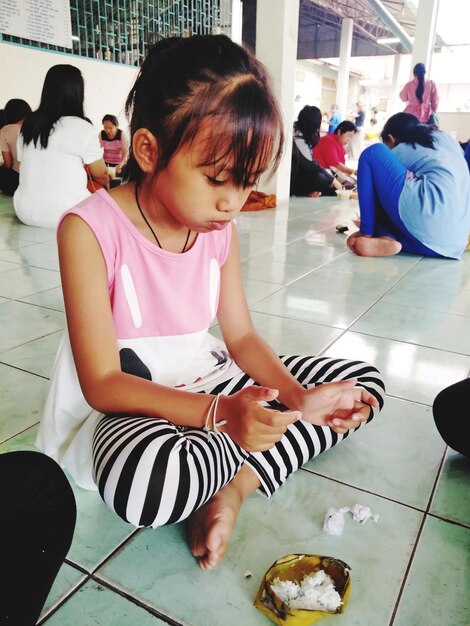 Photo girl with food sitting on tiled floor