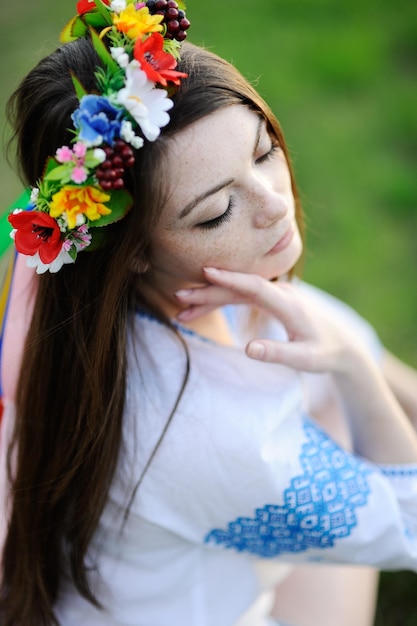 Ragazza con le lentiggini sul viso in una camicia ucraina e bouquet floreale sulla testa