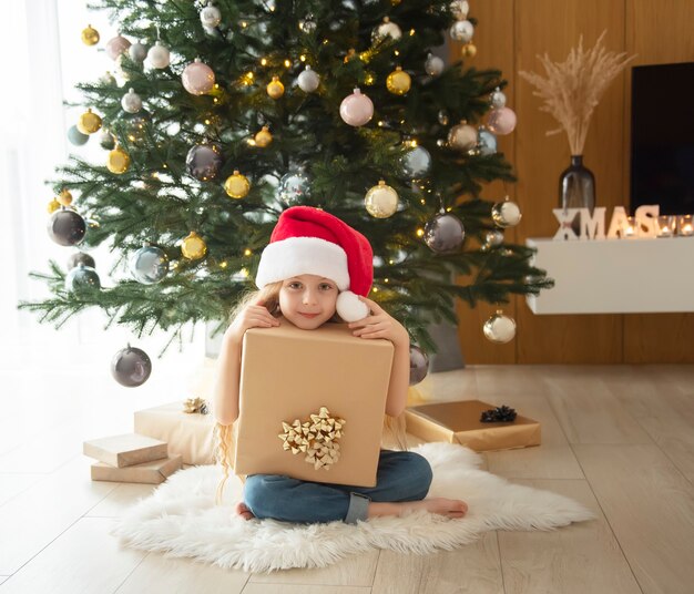 Возле елки играет девочка с подарками. Интерьер гостиной с елкой и украшениями. Новый год. Дарение подарков.