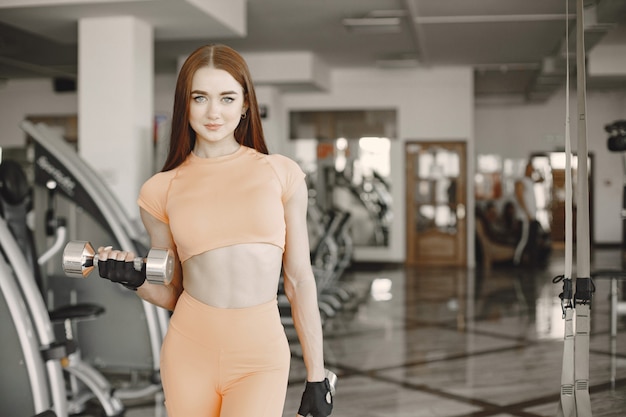 Girl with ginger hair holding two dumbbells. She is at the gym, going to exrcise.